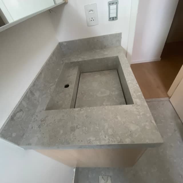 Bancada de banheiro com cuba esculpida: Bancada em pedra cinza com veio miúdo e cuba escavada na própria chapa — sem emenda entre cuba e bancada.