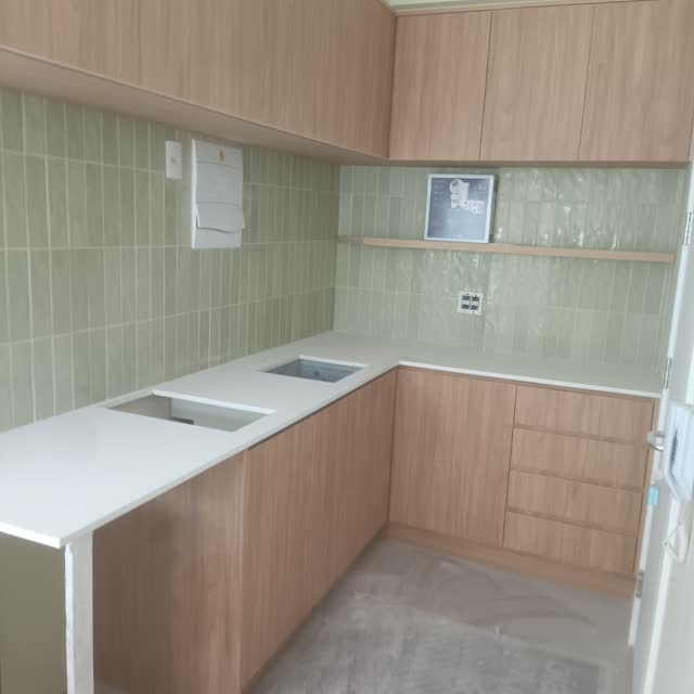 Cozinha em L: Bancada branca em L com duas cubas esculpidas, acompanhando a marcenaria e o azulejo verde.