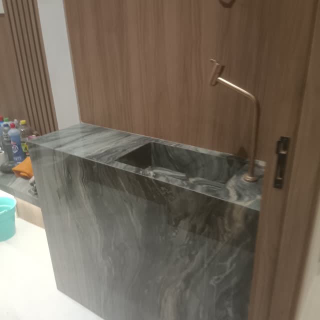 Bancada de banheiro em quartzito: Bancada em quartzito cinza com veio marcado, saia alta e cuba esculpida, com marcenaria ripada ao fundo.