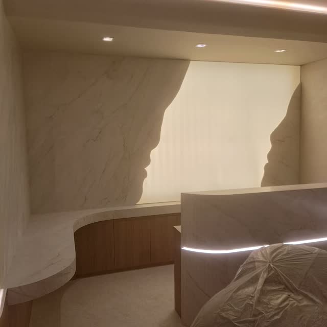 Painel curvo iluminado: Detalhe do painel de mármore claro com borda ondulada e fita de luz acompanhando o recorte.