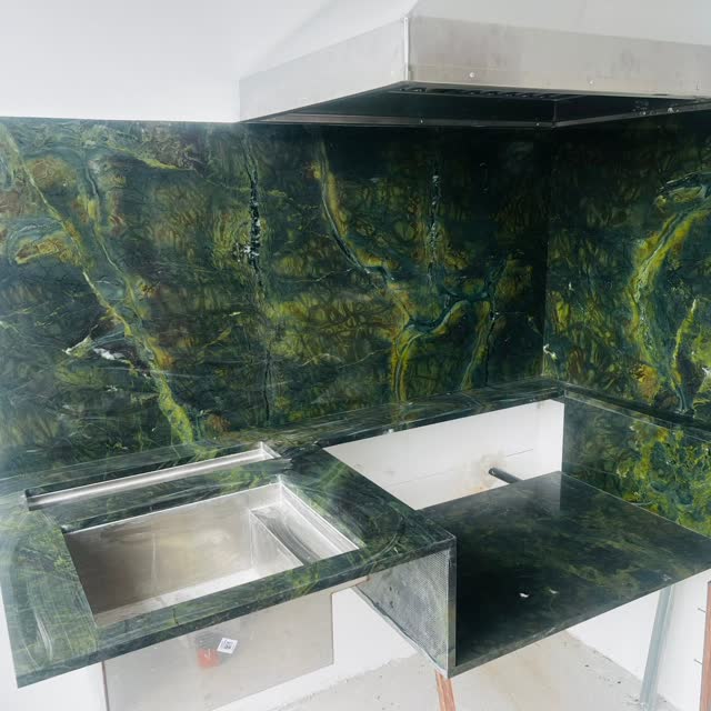 Painel em quartzito verde: Painel e bancada em quartzito verde de desenho exótico, com as faces casadas no encontro das peças.