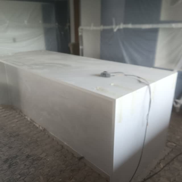 Ilha de cozinha: Ilha em pedra clara com laterais fechadas em peça inteira, aguardando o restante do acabamento.