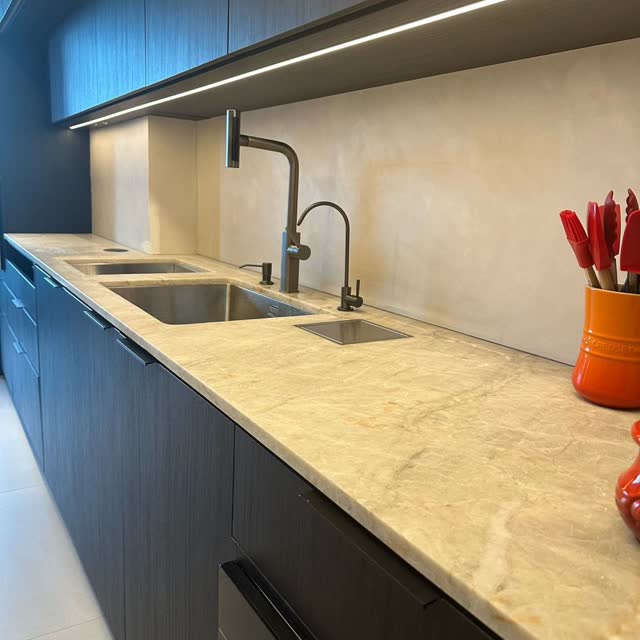 Cozinha com bancada bege: Bancada em mármore bege com duas cubas esculpidas e fundo em peça contínua, com marcenaria azul.