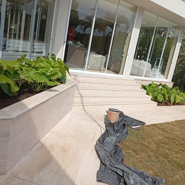 Área externa em travertino: Mureta e piso em travertino contornando o jardim, em residência de alto padrão.