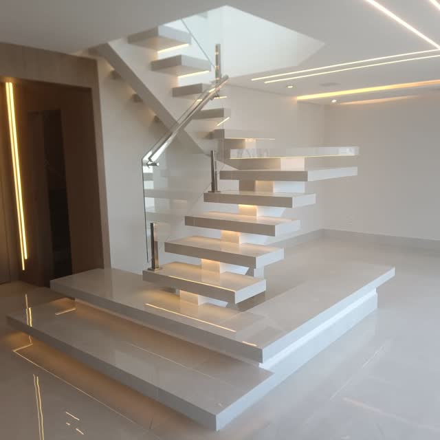 Escada com degraus em balanço: Escada em mármore branco com degraus em balanço e guarda-corpo de vidro, sem estrutura aparente.
