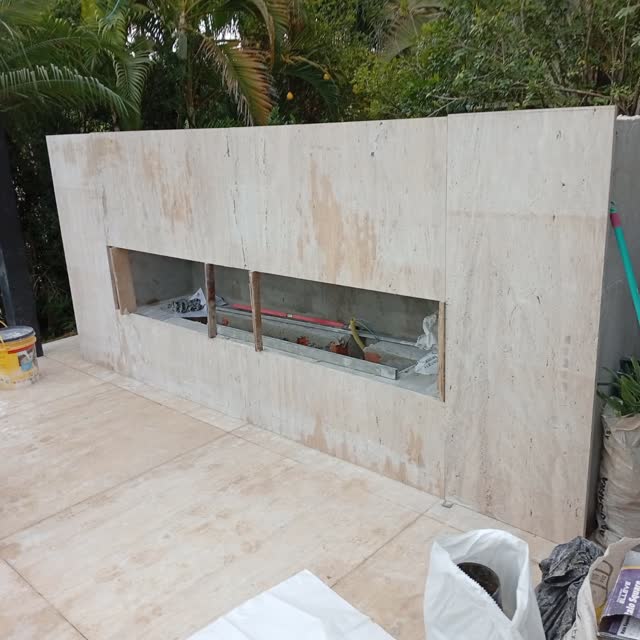 Churrasqueira em travertino: Churrasqueira externa revestida em travertino, com o vão da grelha em construção.