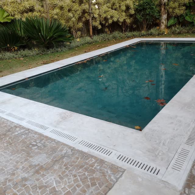 Piscina com borda em travertino: Deck e borda de piscina em travertino, com ralo linear acompanhando o perímetro.