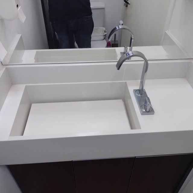 Bancada de lavabo esculpida: Bancada branca com cuba escavada na própria peça e rebaixo para o metal, sem emenda aparente.