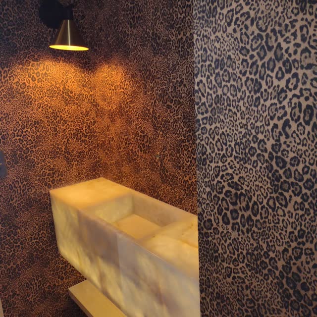 Lavabo em ônix e pedra onça: Cuba de ônix retroiluminada contra parede em pedra de desenho pintado — dois materiais em contraste.