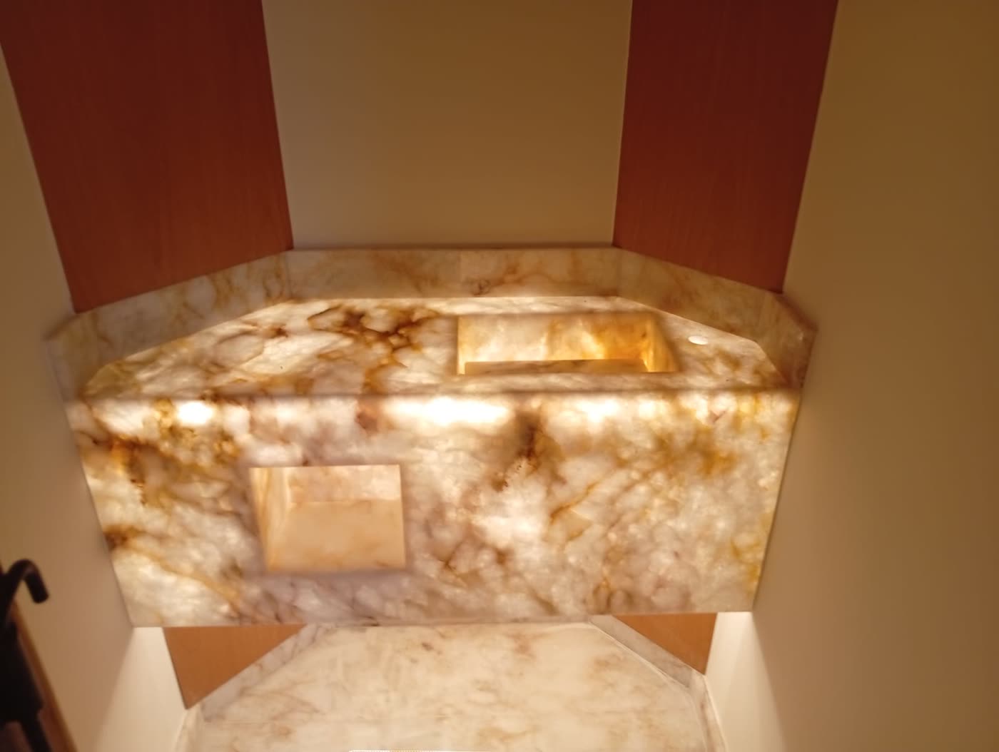 Lavabo revestido em ônix retroiluminado, com bancada e cuba esculpidas no mesmo material.