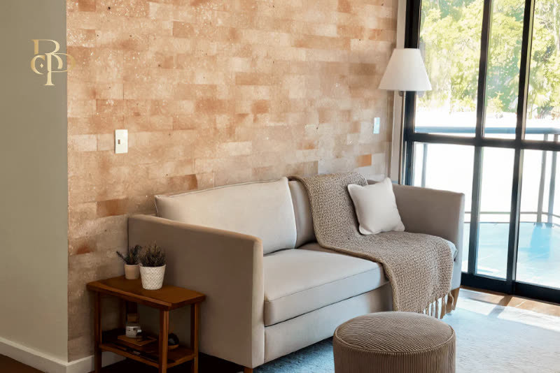 Sala de estar com parede revestida em pedra natural bege-rosada, sofá claro e janela ampla.