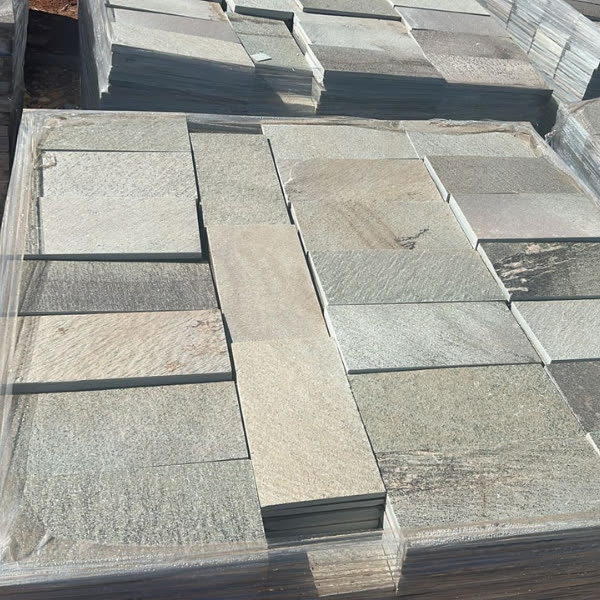 Placas retangulares de pedra cinza-esverdeada em paletes, prontas para aplicação.