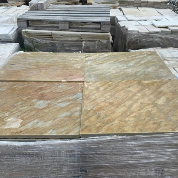 Placas grandes de pedra madeira amarela empilhadas em paletes no pátio.