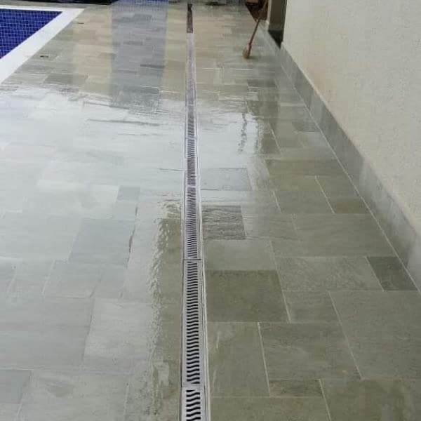 Piso externo em pedra cinza-esverdeada com ralo linear, ao lado de piscina.